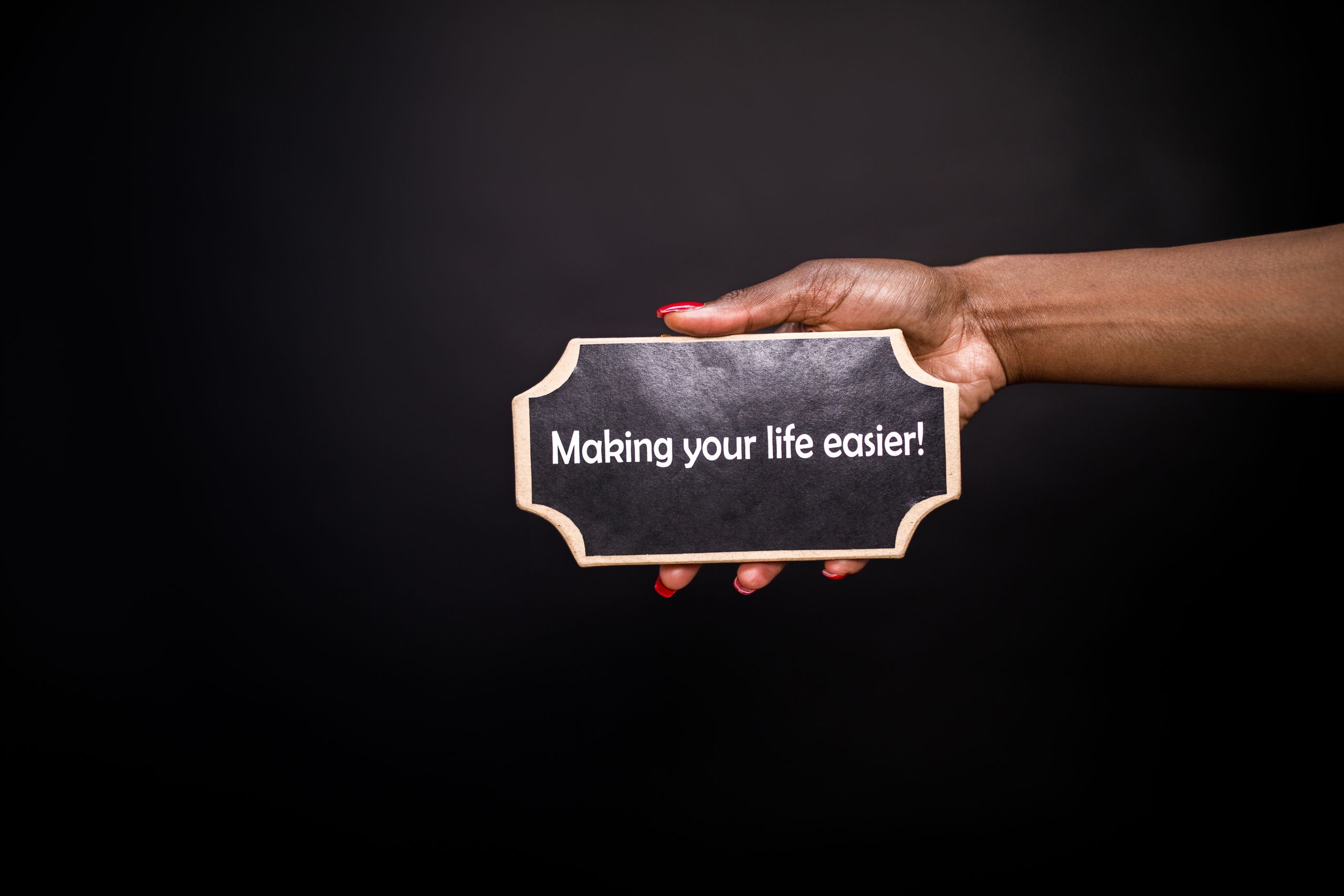 A hand holding a sign with the quote 'Making your life easier!' against a black background.