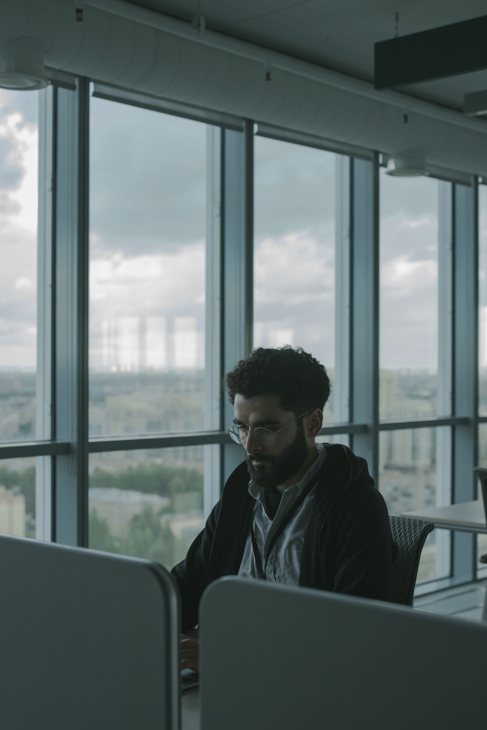 A man in a black jacket is working in a modern office with panoramic city views.