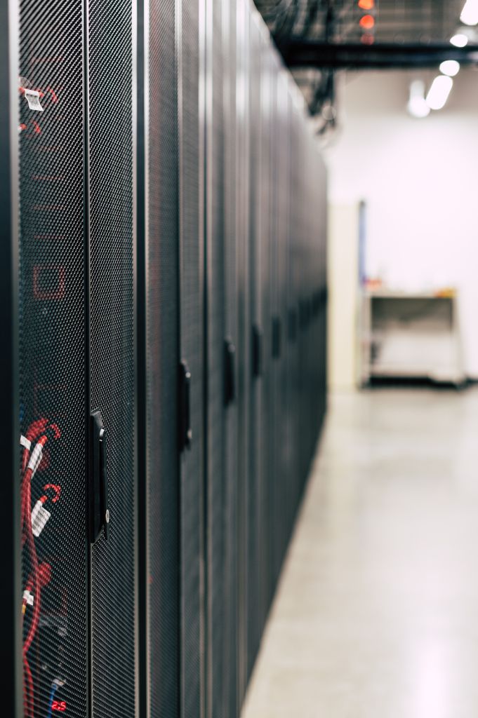 Microsoft 365 Metal black cabinets with servers inside with red wires connected standing in row in lighted room